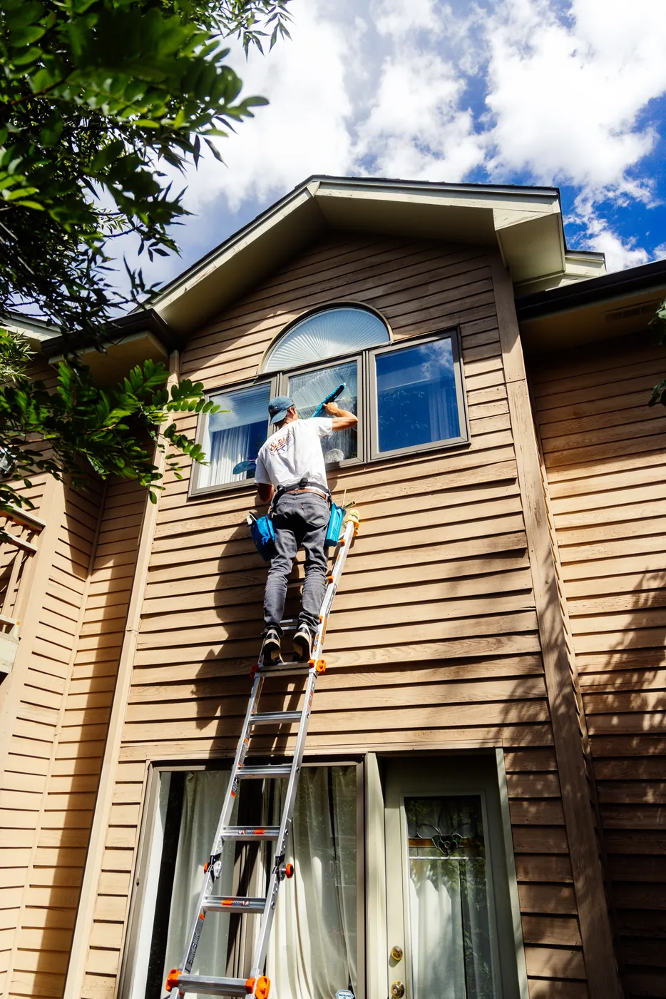 Sunshine Window Works technician on a ladder cleaning upper-story windows on a two-story home