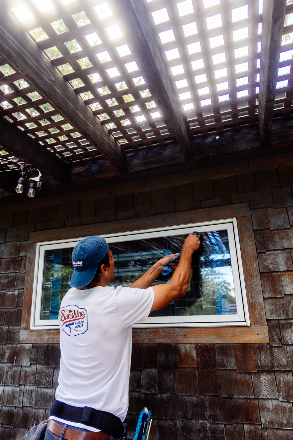 Technician cleaning a hard-to-reach window tucked beneath a pergola