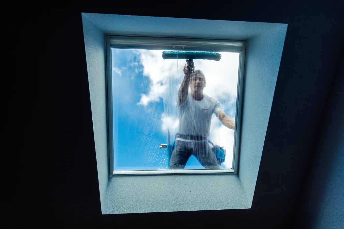 Skylight being cleaned from below, reflecting blue sky and clouds