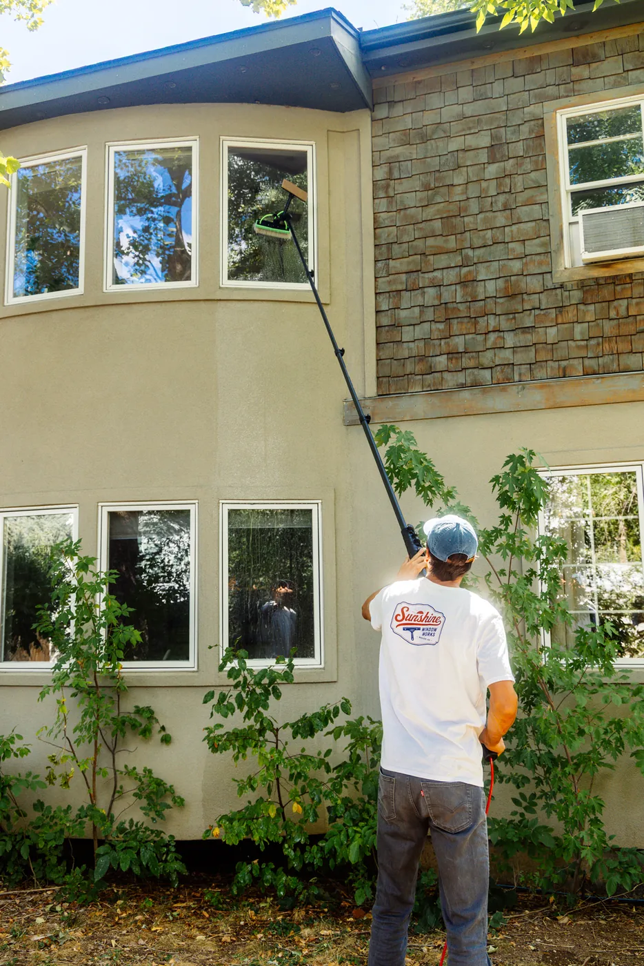Sunshine Window Works technician using a water-fed pole to clean upper-story bay windows on a two-story Boulder home